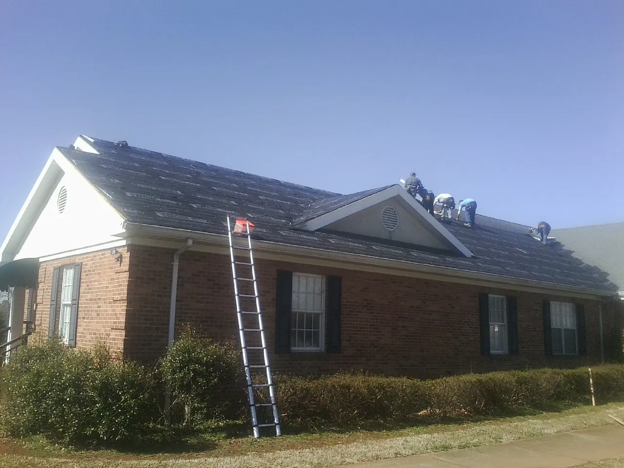 Crew tearing shingles off a brick ranch roof with a ladder set — Metal Roof Repair work by our crew in Winchester